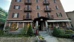 A multi-story building with balconies, a central entrance, and a garden area with plants. - Hotel Appennino (Fiumalbo)