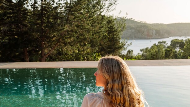 Eine Person steht an einem Pool mit Blick auf Bäume und Hügel.
