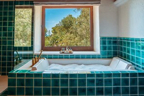 Ein Badezimmer mit einer Badewanne, einem Fenster mit Blick auf Bäume und grünen Fliesenwänden.