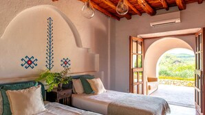 Ein Schlafzimmer mit zwei Betten, einer Pflanze und Blick durch eine offene Tür.