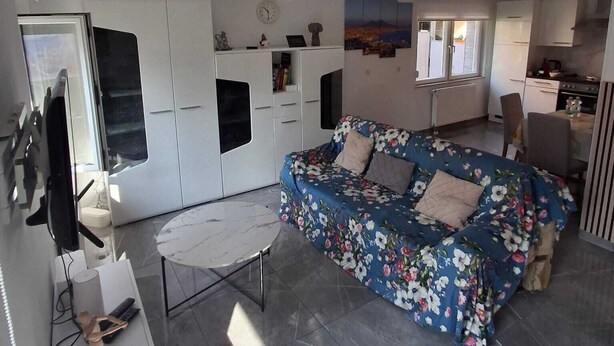 A living room with a sofa, a TV, a small table, and a kitchen area with cabinets and a stove. - Vacation apartment in Bönnigheim, detached house near Tripsdrill adventure park (Bönnigheim)