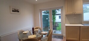 A dining area with a glass table, chairs, and a view through a glass door to the outside.