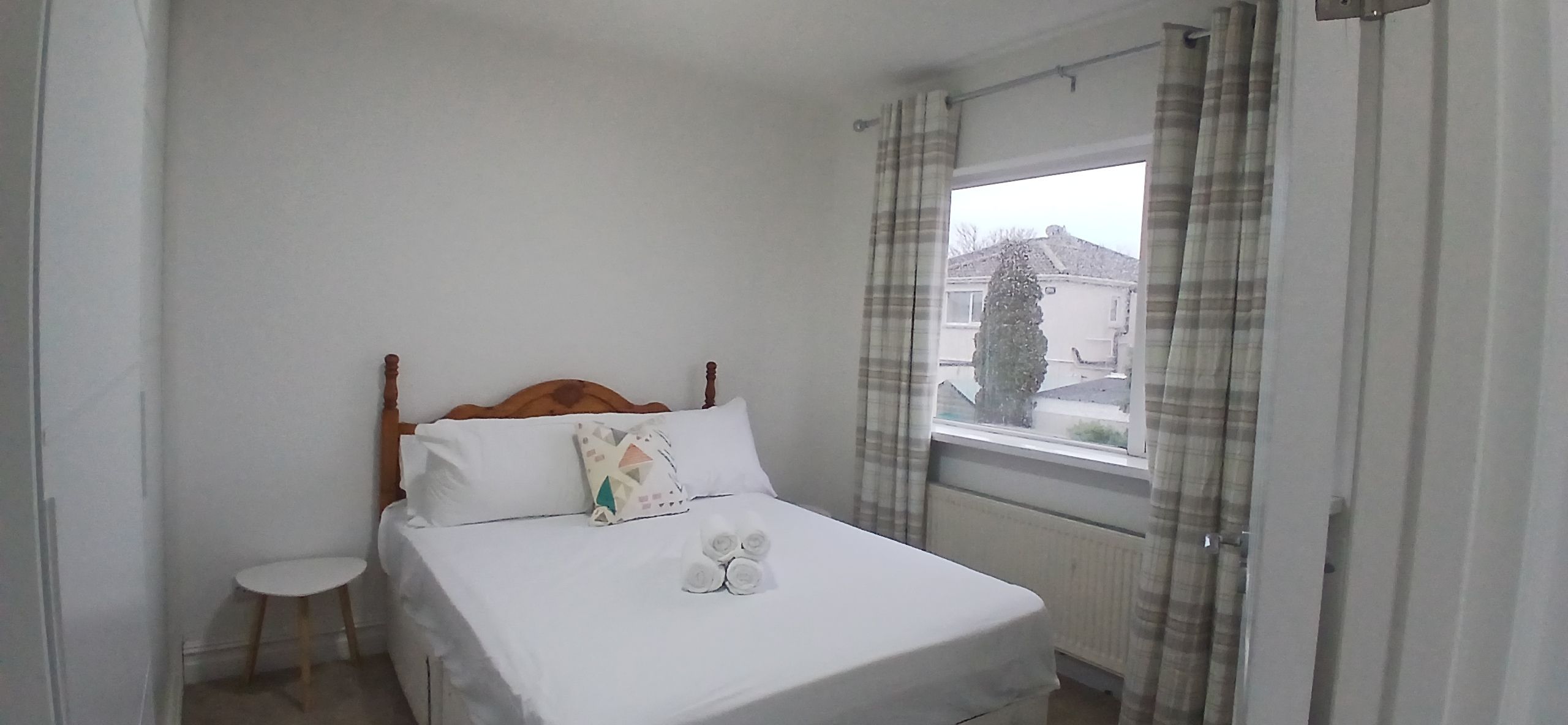 A neatly made bed with a wooden headboard, a small bedside table, and a window with curtains.