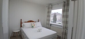 A neatly made bed with a wooden headboard, a small bedside table, and a window with curtains. - Fresh Stylish 3BDR Home with Garden Near City (Dublin)