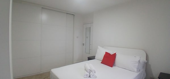 A hotel room with a bed, a red pillow, a white pillow, and a white towel.