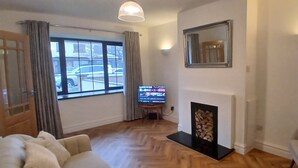 Ein Wohnzimmer mit Kamin, Fernseher und einem fensterbepflanzten Fenster.