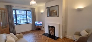 A living room with a fireplace, a television, and a window with curtains.
