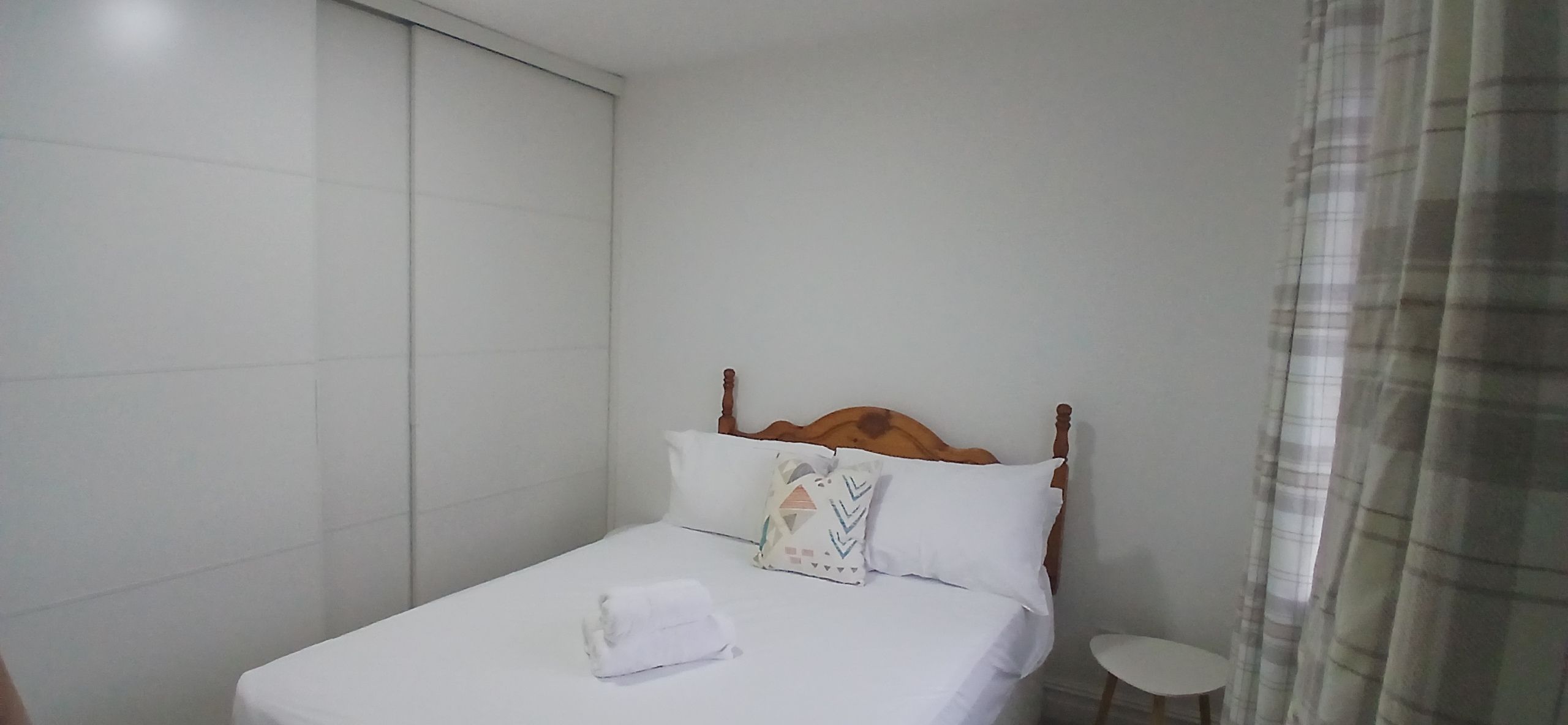 A hotel room with a bed, a bedside table, and a curtain.