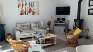 Ein Wohnzimmer mit einer Couch, zwei Korbstühlen, einem Couchtisch, einem Flachbildfernseher, einem Kamin und einem Bild an der Wand.