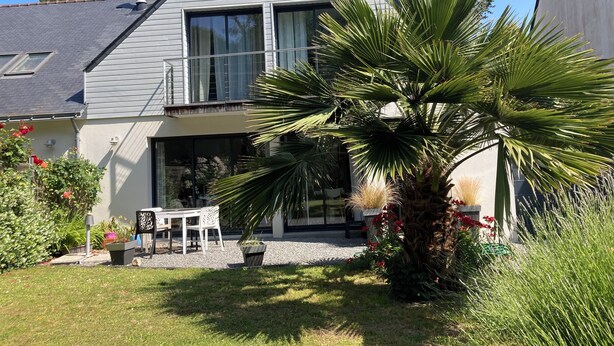 Ein zweistöckiges Haus mit Balkon, einer Terrasse mit Tisch und Stühlen sowie einer großen Palme.