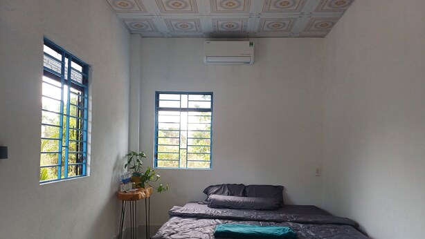 A bedroom with a bed, two windows, a potted plant, and an air conditioning unit. - Beautiful 3-bedroom villa with AC in charming Phú Quốc (PHÚ QUỐC)