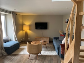 Una sala de estar moderna con un sofá, una mesa redonda de madera, una lámpara de pie, un televisor y una escalera.