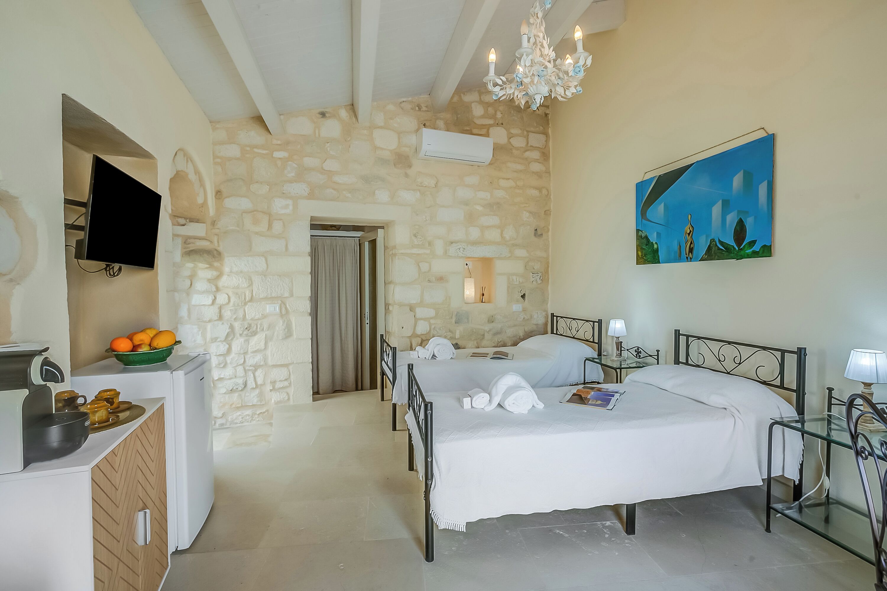 Une chambre avec un mur en pierre, un lit, un bureau avec un panier de fruits, une télévision et un tableau.