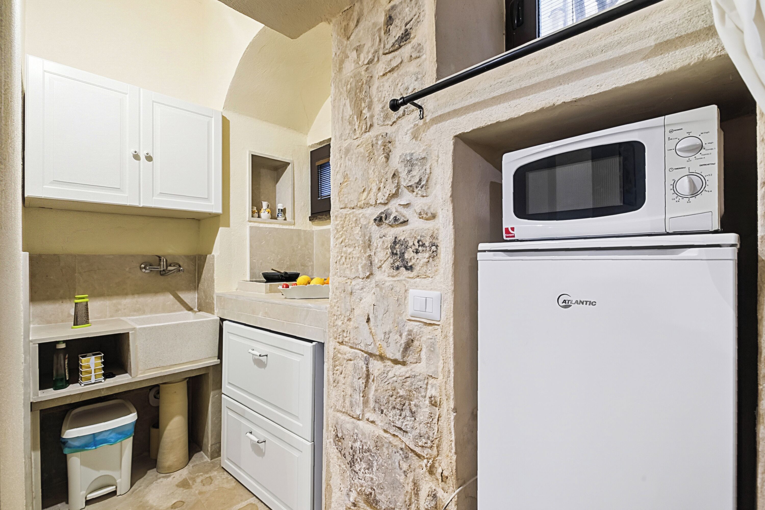 A compact kitchen with white cabinets, a stone wall, a microwave, and a refrigerator.