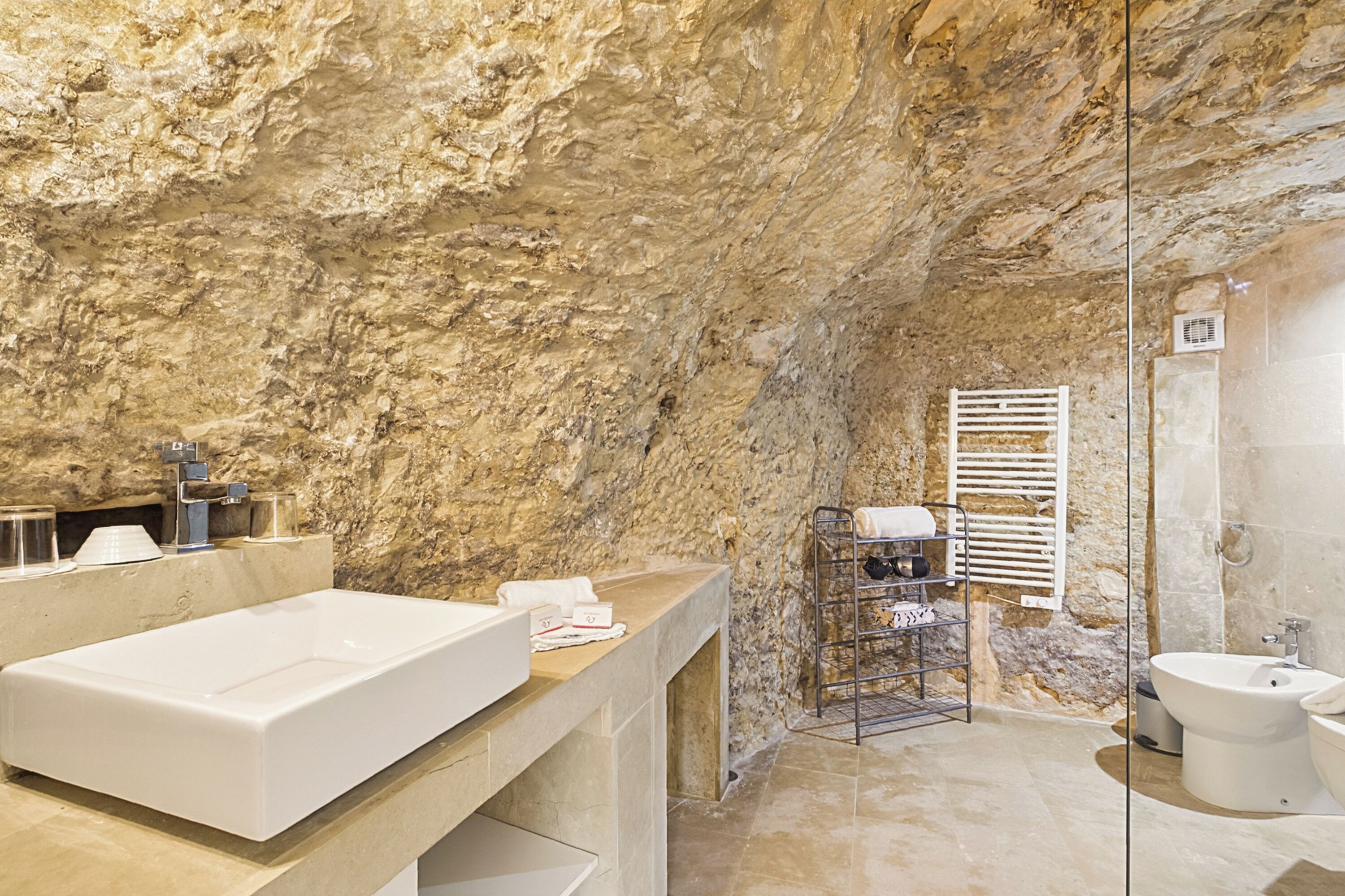 A bathroom with a stone wall, a large bathtub, a sink, and a bidet.