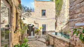 A stone courtyard with a pool, potted plants, and a sign for 'Palestra Fitness Room.'