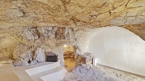 A cave-like interior with a glass table, white walls, and a staircase leading to a door.