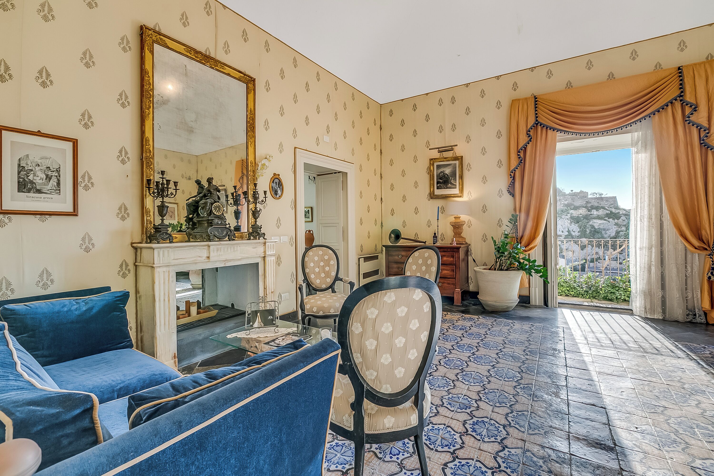 A room with a fireplace, blue sofa, patterned floor, and a view through a window.