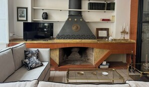 Een woonkamer met een open haard, een bank, een bijzettafeltje en een televisie.