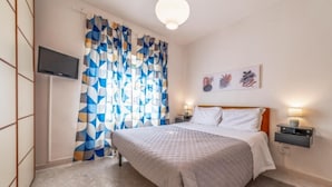 Une chambre à coucher comprenant un lit, un téléviseur, une table de chevet, une lampe et un rideau orné d’un motif géométrique.