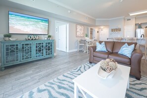 A living room with a TV, a brown sofa, a white coffee table, and a teal cabinet. - Beach Chair Service Included - Gulf front Master - Bunk Room - Near Pier Park (Panama City Beach)