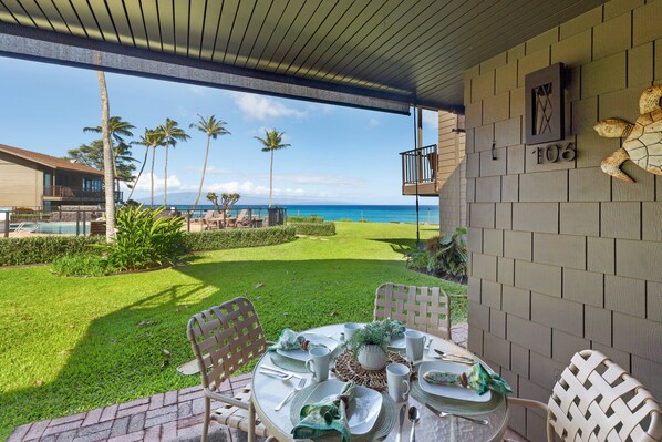 A patio with a table set for dining, overlooking a lawn with palm trees and a view of the ocean. - SUMMER SALE! Ocean View Paradise,1BR condo in Lahaina - Polynesian Shores 106 (Lahaina)