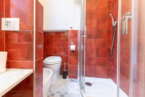 Ein Badezimmer mit roten Fliesen, einer Toilette, einer Badewanne und einer Duschkabine mit Glastüren.