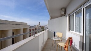 En balkon med et bord og stole, et vindue og udsigt til bygninger i det fjerne.