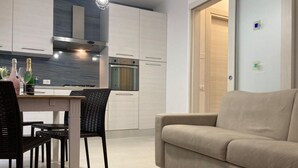 Eine moderne Küche mit weißen Schränken, ein Essbereich mit Tisch und Stühlen und ein beiges Sofa in einem Wohnbereich.
