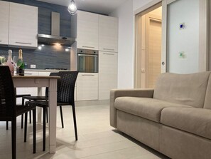 Eine moderne Küche mit weißen Schränken, ein Essbereich mit Tisch und Stühlen und ein beiges Sofa in einem Wohnbereich.