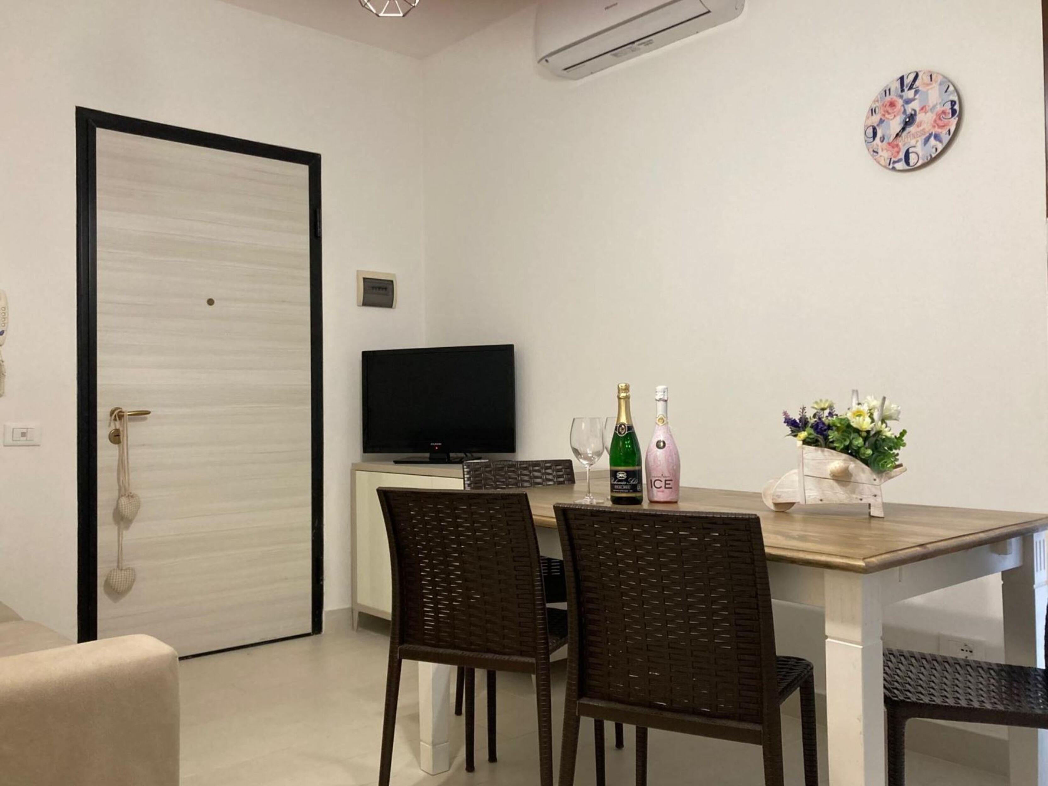 A dining area with a table, chairs, a television, and a clock on the wall.