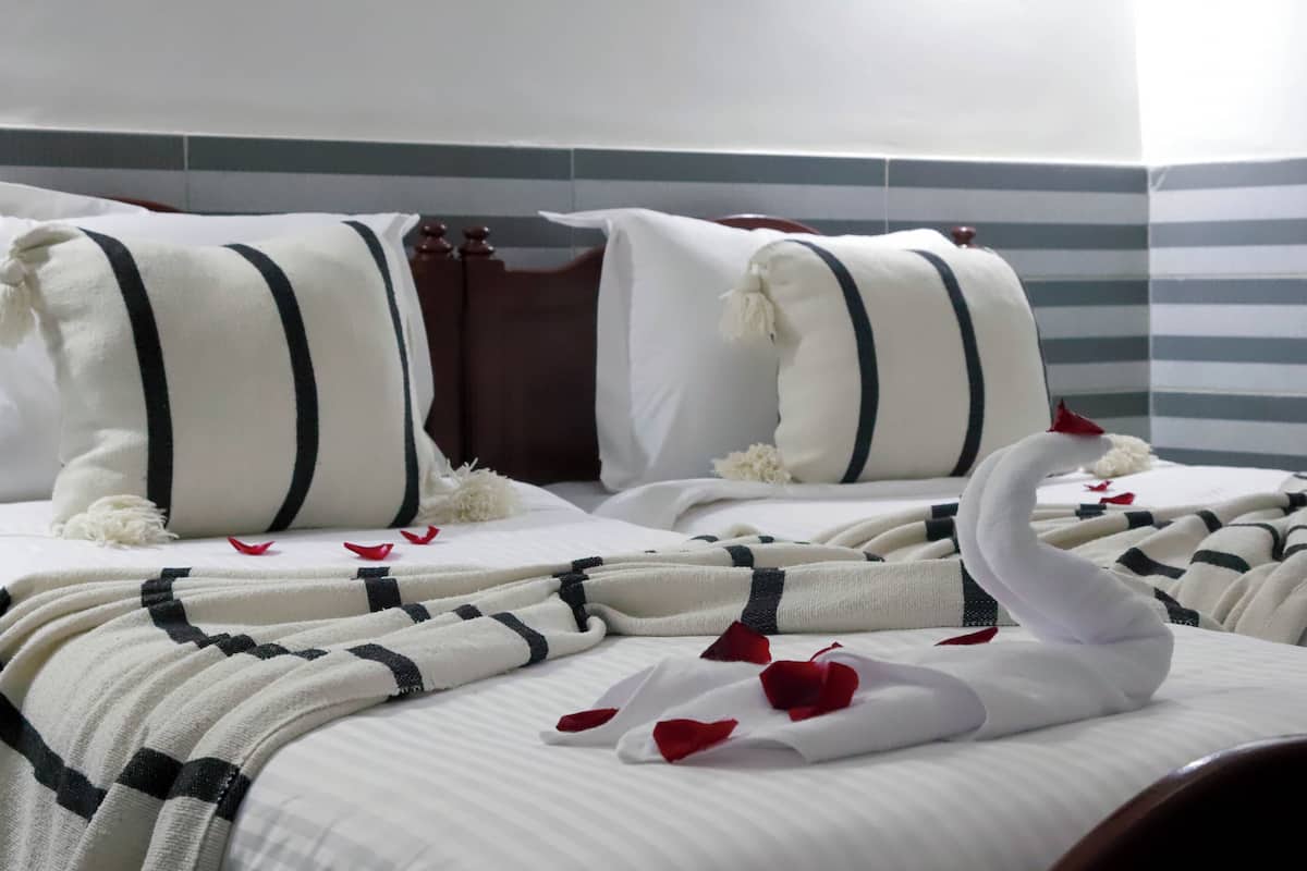 A hotel room with two beds, striped headboards, white bedding, and decorative swan pillows.