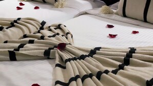 A bed with a white and black striped blanket, red rose petals scattered on the bed, and a white pillow. - Riad Allal (Marrakech)