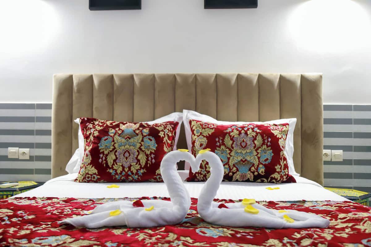 A hotel room with a bed, two decorative pillows, and a swan-shaped pillow arrangement.