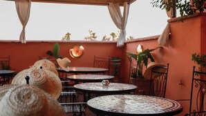 An outdoor patio with round tables, chairs, and a decorative wall. - Riad Allal (Marrakech)