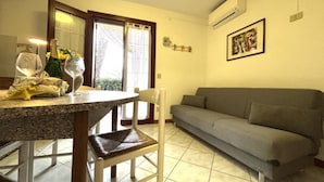 A living room with a dining table, a sofa, and a chair. - Flat in Seafront Residence With Pool (Rosolina)