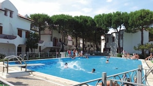 A swimming pool surrounded by buildings with balconies, trees, and a clear sky. - Flat in Seafront Residence With Pool (Rosolina)