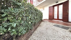 A building with a gravel pathway, a wooden door, and a metal railing on the balcony. - Flat in Seafront Residence With Pool (Rosolina)