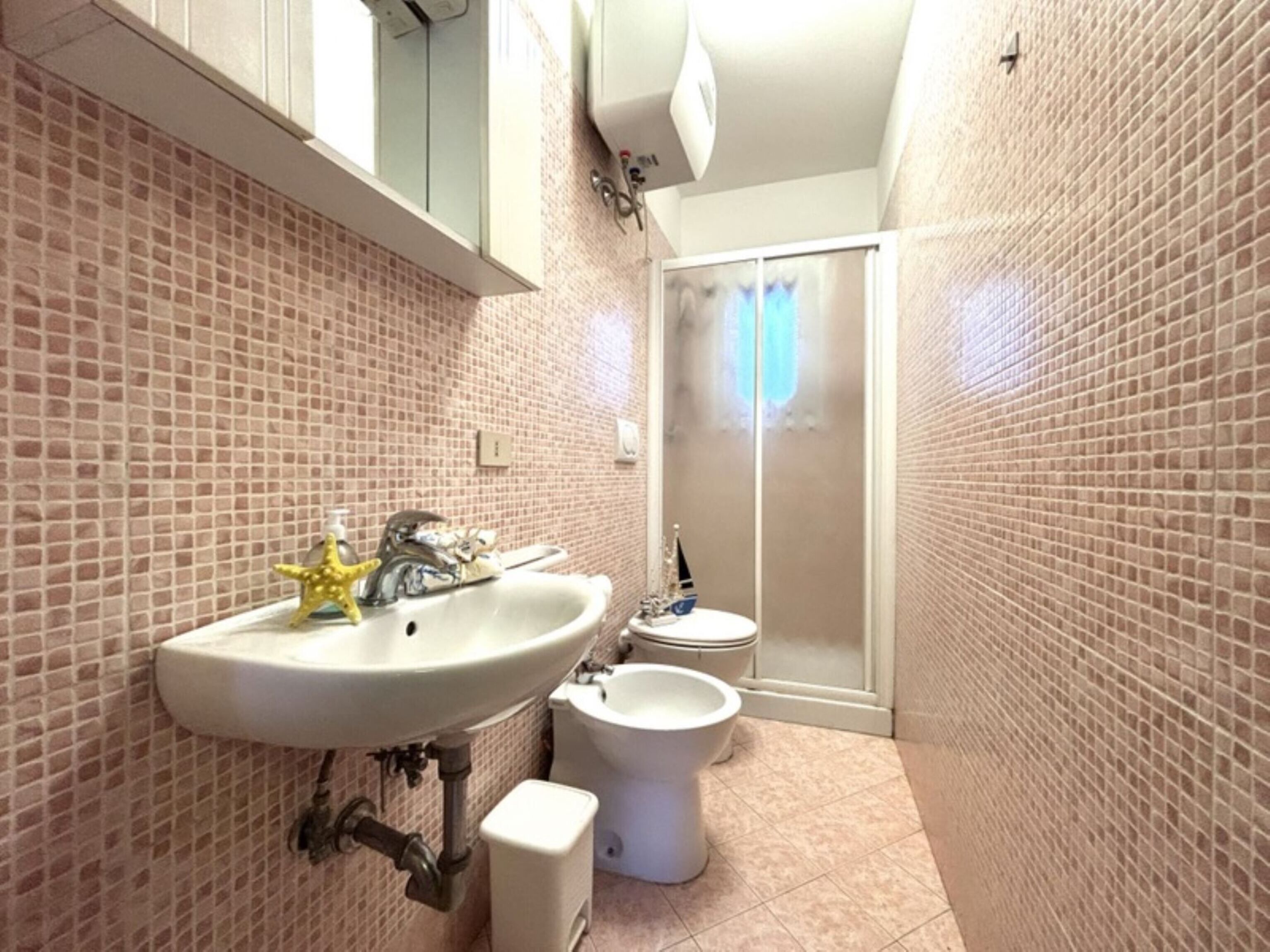 Une salle de bain comprenant un lavabo, un bidet et des toilettes, avec des murs carrelés et un espace douche.