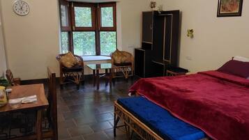 Une pièce comprenant un lit, une table, deux chaises, une armoire et une fenêtre donnant sur un paysage verdoyant.