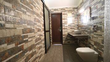 A bathroom with a stone-patterned wall, a wooden door, a sink with a vessel basin, and a toilet.
