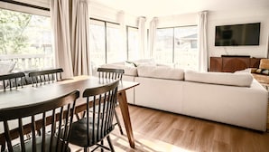 A room with a dining table, chairs, a sofa, a TV, and large windows. - The Family Clubhouse at Abbey Springs (Fontana)
