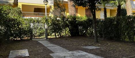 A courtyard with a paved walkway, a metal gate, and a yellow building with balconies.