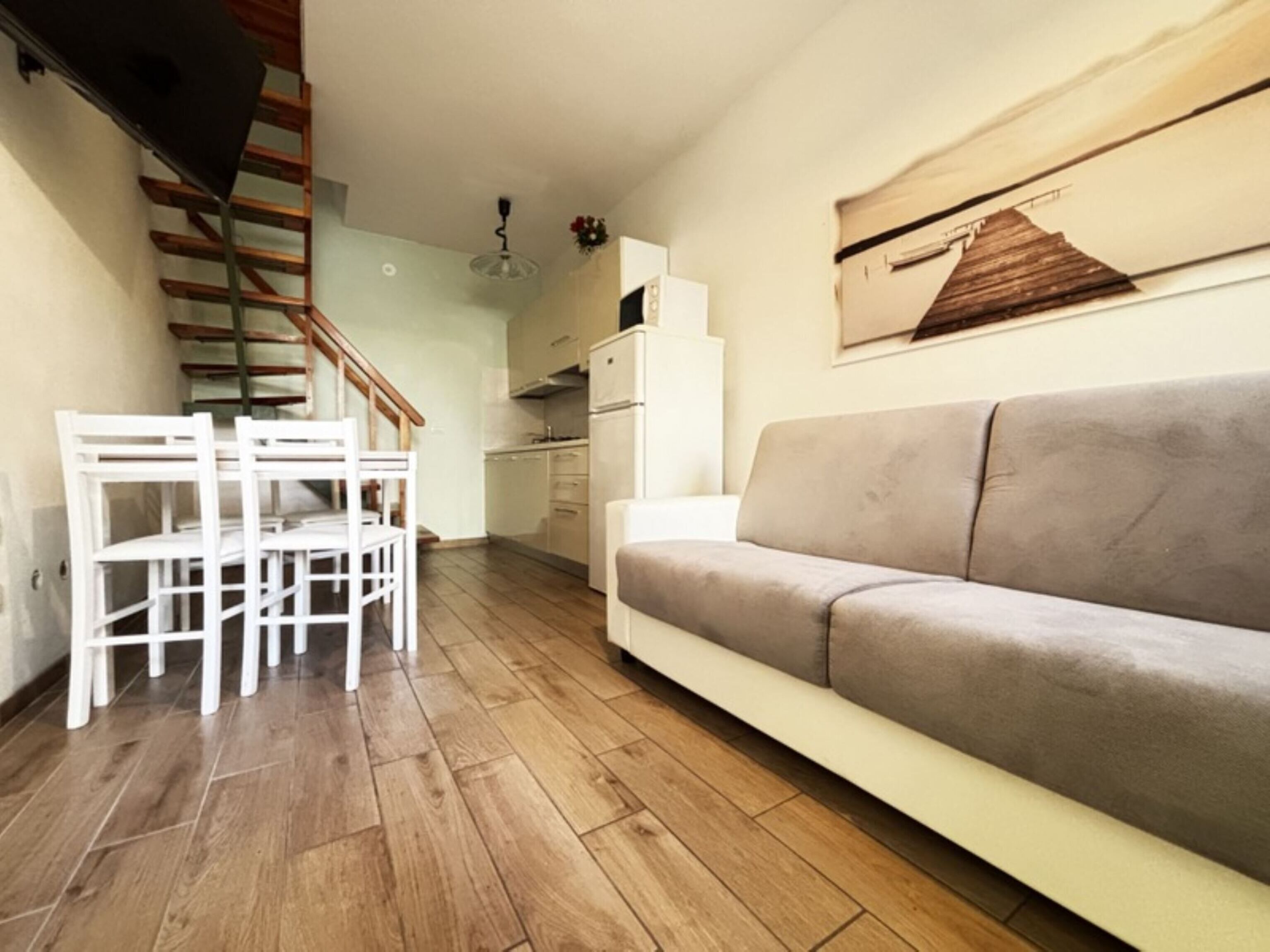 Uma sala de estar com sofá, uma mesa de jantar com cadeiras, uma área de cozinha e uma escada.