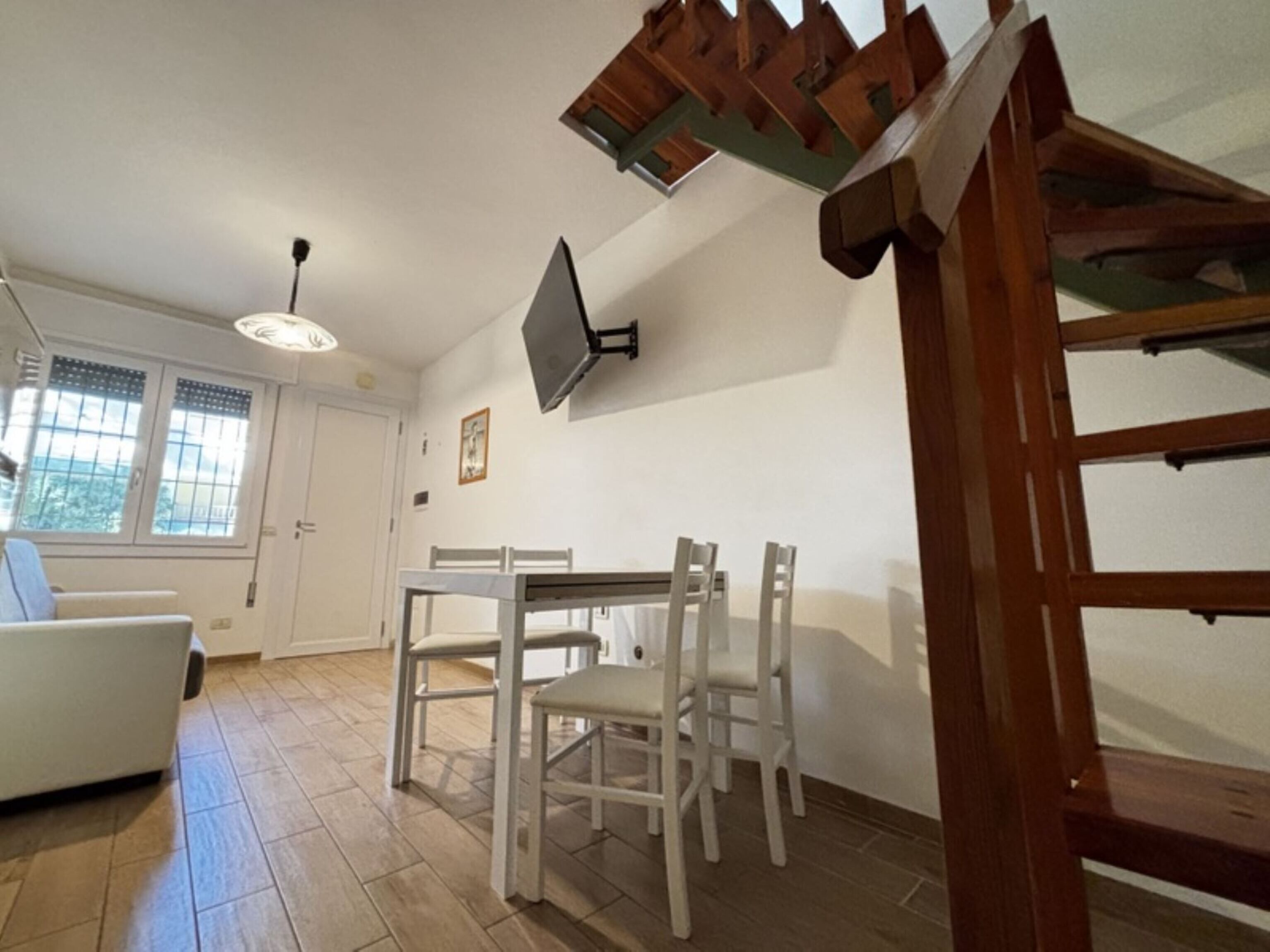 A dining area with a table and chairs, a ceiling fan, a window with blinds, and a staircase.