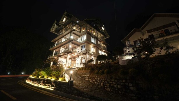 A multi-story building with balconies, a stone retaining wall, and a well-lit entrance. - Longitude Homestay (Kalimpong)