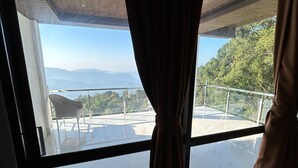A room with a large window, curtains, and a view of a balcony with a railing. - Longitude Homestay (Kalimpong)