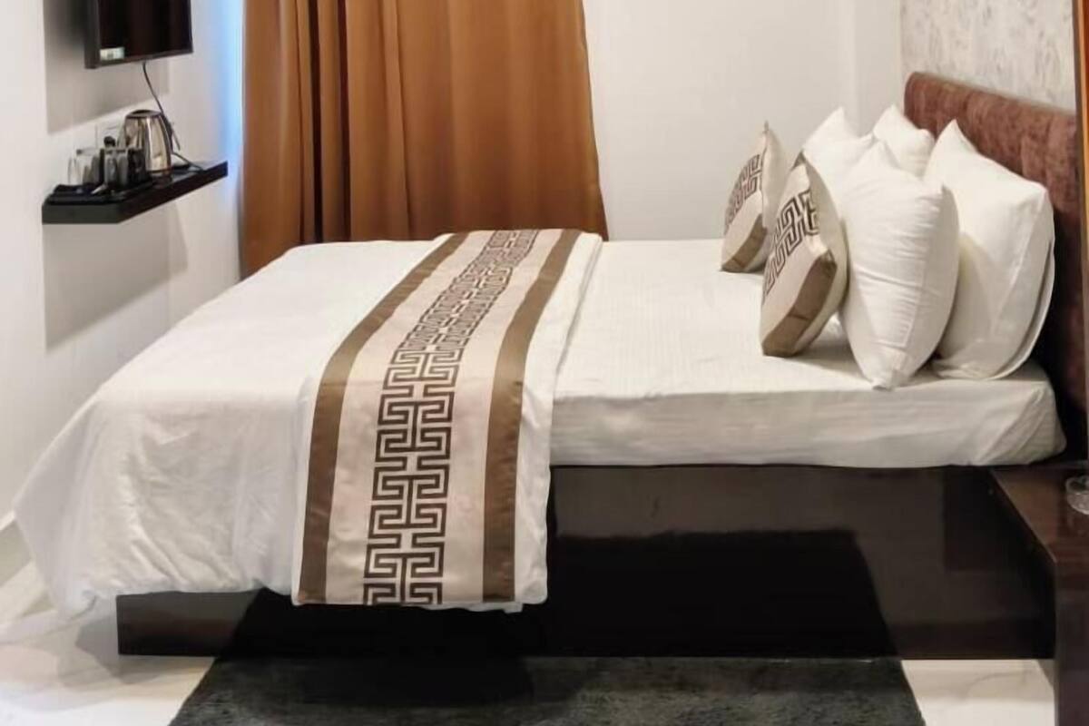 Une chambre d’hôtel équipée d’un lit, d’un téléviseur à écran plat, d’une table de chevet et d’une fenêtre avec des rideaux.