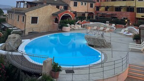 Una piscina con una barrera de cuerda, sillas de descanso y un edificio con varios balcones.