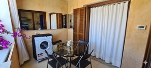 A compact balcony with a washing machine, a glass table with chairs, and a view of the kitchen through a mirror. - Apartment 'C 210 Puntavilla' with Shared Pool, Wi-Fi, and Air Conditioning (La Maddalena)